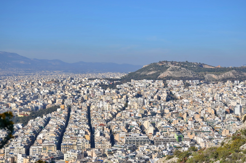2 - A high-angle panoramic view over the dense urban sprawl of Athens, Greece, looking toward the Tourkovounia hills from an elevated vantage point like Mount Lycabettus